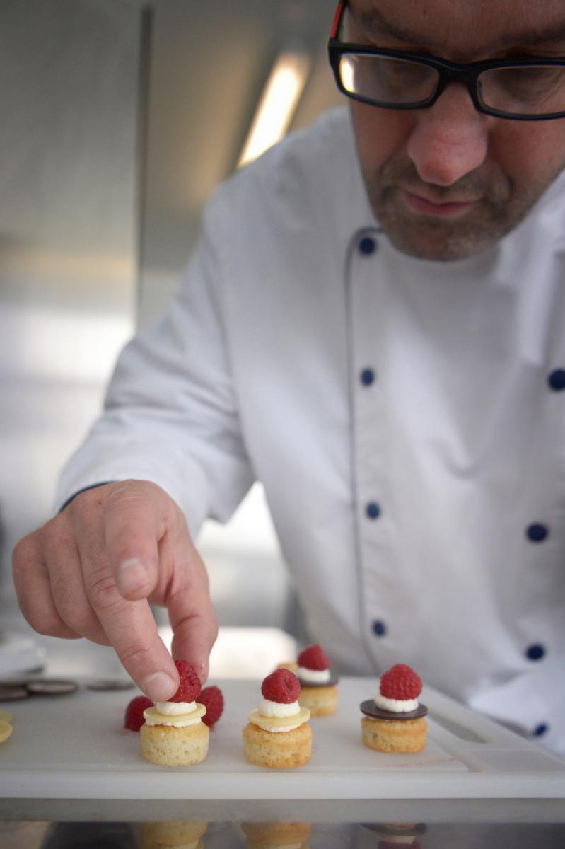 Chef pâtissier déposant une framboise sur une pièce cocktail sucrée lors d’une fabrication artisanale en Bretagne.