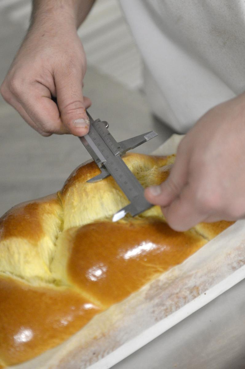 Mains utilisant un pied à coulisse pour mesurer une brioche tressée dans une unité de production agroalimentaire.