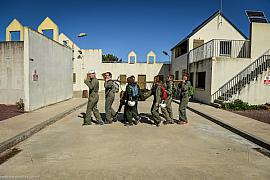 Groupe d’hommes portant un brancard en bois lors d’un exercice de leadership en plein air sous un soleil vif.