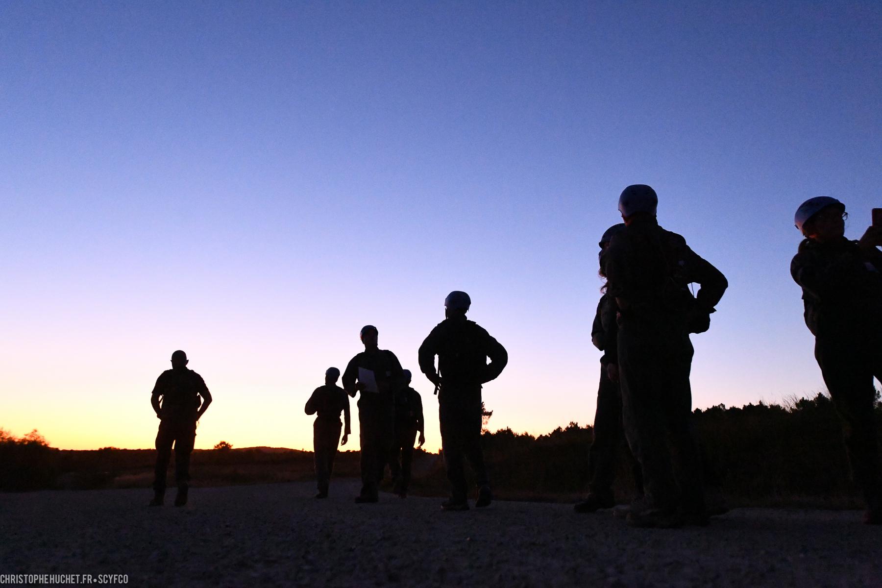 Silhouettes de stagiaires casqués lors d’un entraînement au crépuscule sous un dégradé de ciel bleu et orange.