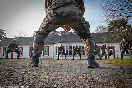 Participants en tenue camouflage et casques bleus effectuant des squats devant un bâtiment blanc typique en Bretagne.