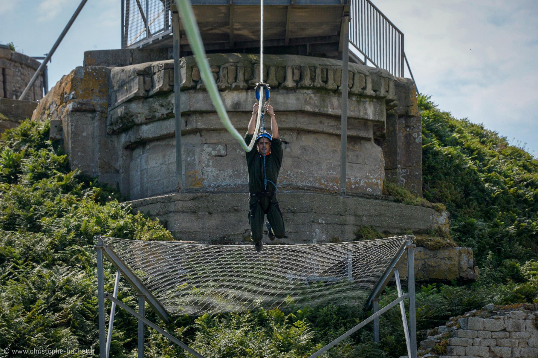 Homme suspendu à une corde de tyrolienne, au-dessus d’un filet devant des fortifications de pierre 