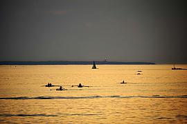 Silhouettes de plusieurs avirons naviguant sur une mer calme et dorée par le coucher de soleil à Saint-Malo