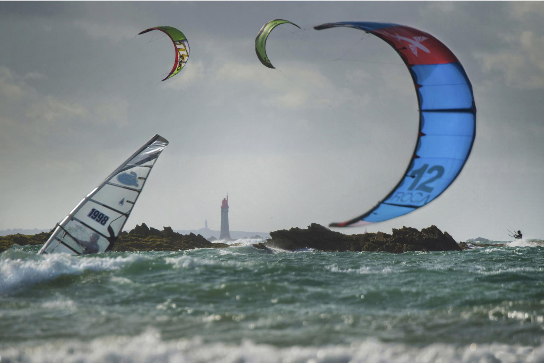 Ailes de kite et voile de windsurf sur mer agitée avec phare au loin sous un ciel nuageux à Saint-Malo.