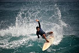 Surfeur en plein virage sur une vague avec d’importantes projections d’écume blanche et eau turquoise.