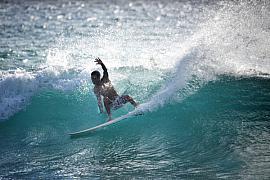 Surfeur en pleine action sur une vague de l’océan Indien à Boucan Canot, lumière vive et projections d’eau.