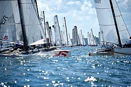 Multiples voiles de catamarans en mer. Lumière vive, reflets sur l’eau et départ de course nautique.