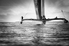 Photographie Photographe nautique et voile, je capte l'immersion au cœur d'une régate de mulicoques. Une œuvre en noir et blanc illustrant la beauté des bateaux volants au dessus de l'eau