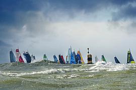 Nombreux voiliers IMOCA aux voiles colorées franchissant des vagues écumeuses sous un ciel nuageux au Havre.