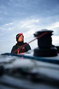 Marin avec lampe frontale sur son voilier Mini 6.50 au crépuscule en mer, winch au premier plan flou