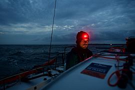 Skipper portant une lampe frontale rouge à bord d’un voilier Mini 6.50 en mer agitée au crépuscule en Bretagne.