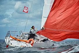 Skipper manœuvrant un voilier Mini 6.50 avec spinnaker rouge sur mer agitée en Bretagne.