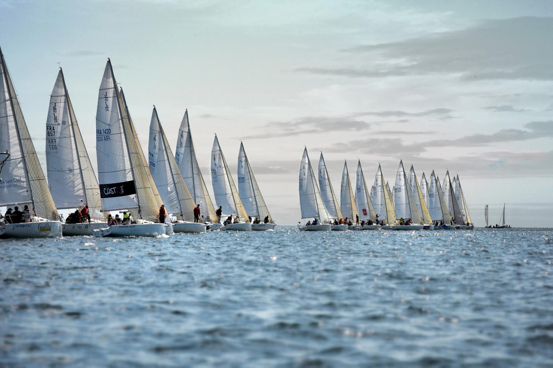 Alignement de voiliers J80 sur mer calme en Bretagne sous un ciel clair lors d’une compétition nautique.