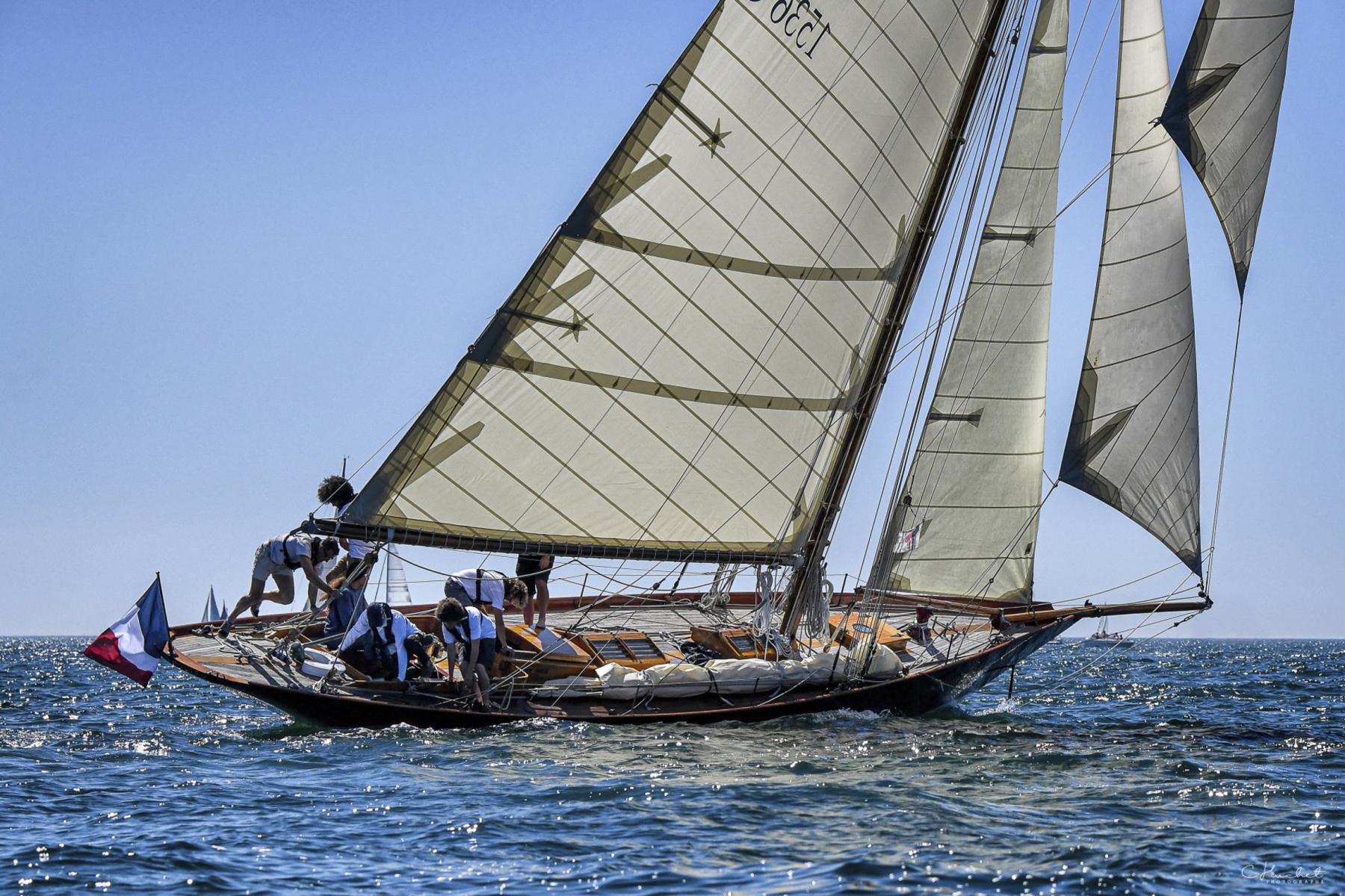 Voilier classique Pen Duick naviguant sous voiles blanches avec équipage actif sur le pont en bois.