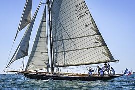 Voilier classique Pen Duick I avec voiles blanches déployées sur mer calme sous un ciel bleu azur