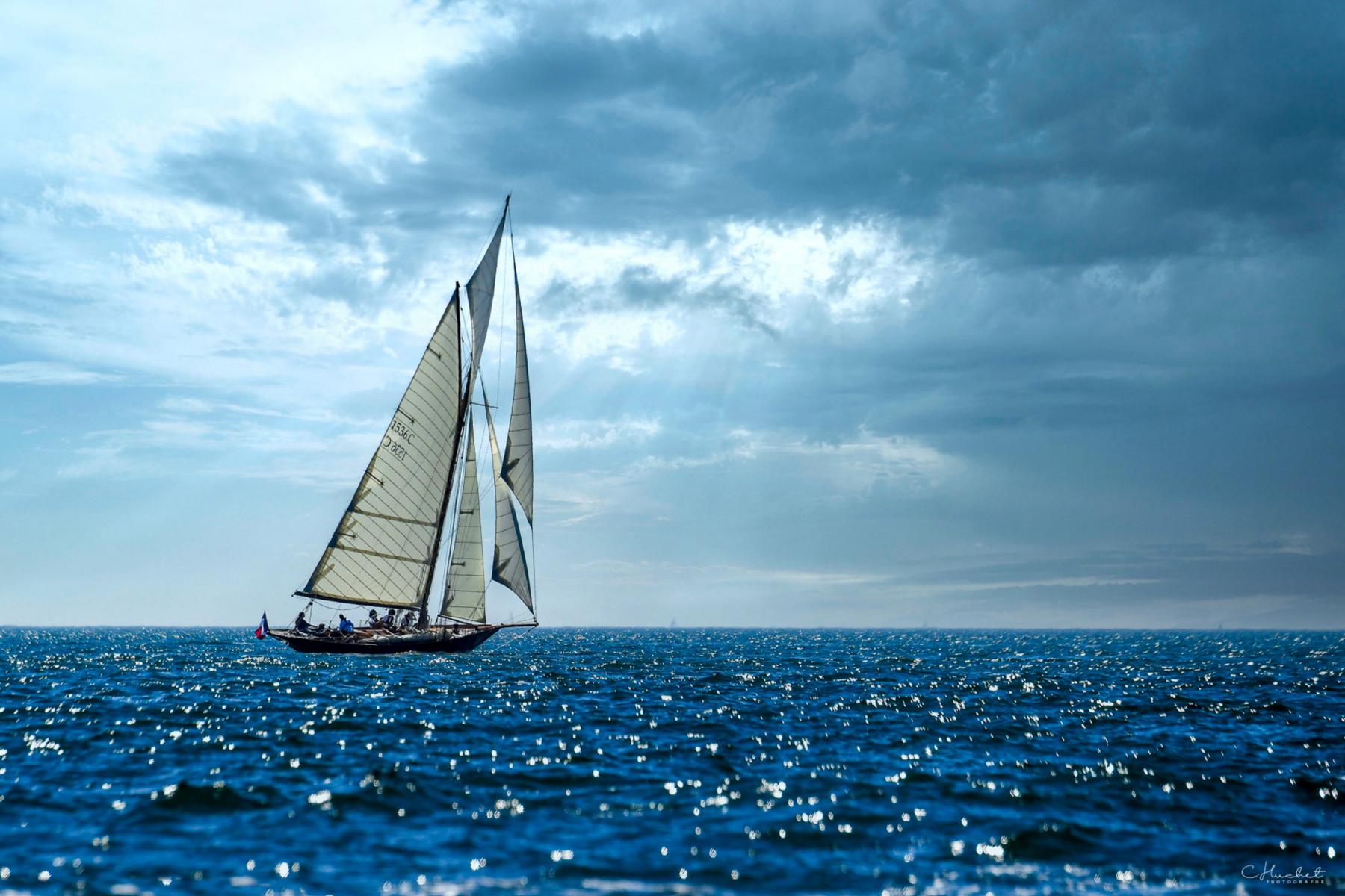 Pen Duick 1 naviguant toutes voiles dehors sur mer scintillante Bretonne et sous un grand ciel chargé de nuages