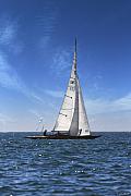 Voilier en bois à coque sombre avec grande voile blanche sur mer bleue scintillante sous ciel azur ensoleillé.