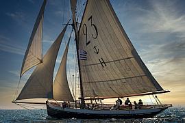 Vieux gréement Marie Fernand, voiles beiges déployées, naviguant en mer sous une lumière dorée de fin de journée.
