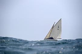 Vieux gréement à voiles blanches naviguant sur une mer agitée sous un ciel clair. Focus sur la gîte du bateau.