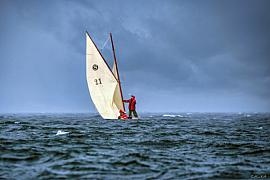 Marin en ciré rouge sur un vieux gréement à voiles blanches par temps d’orage en mer de Bretagne.