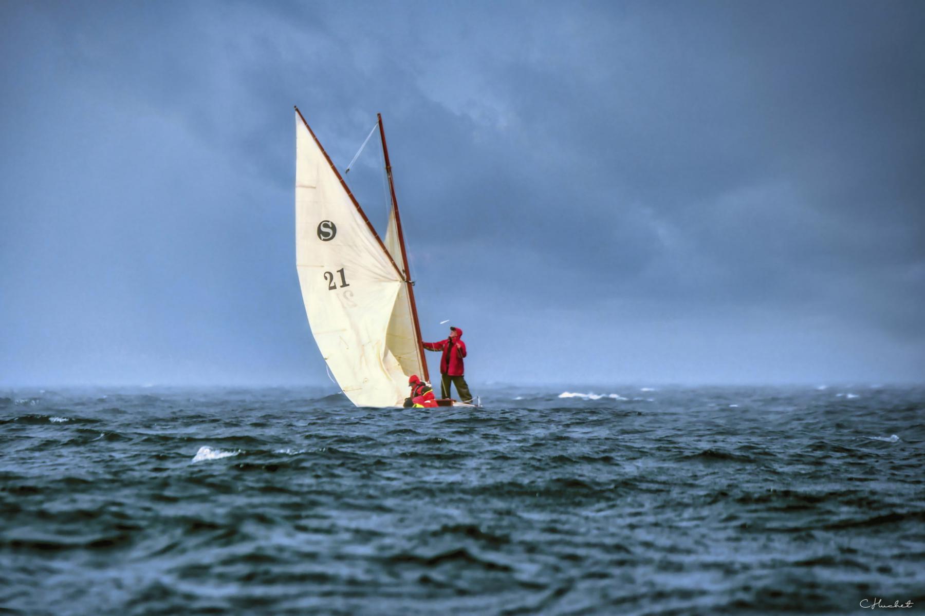 Marin en ciré rouge sur un vieux gréement à voiles blanches par temps d’orage en mer de Bretagne.