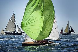 Dériveur 505 avec spi vert gonflé naviguant devant des vieux gréements en bois sur une mer bleue ensoleillée