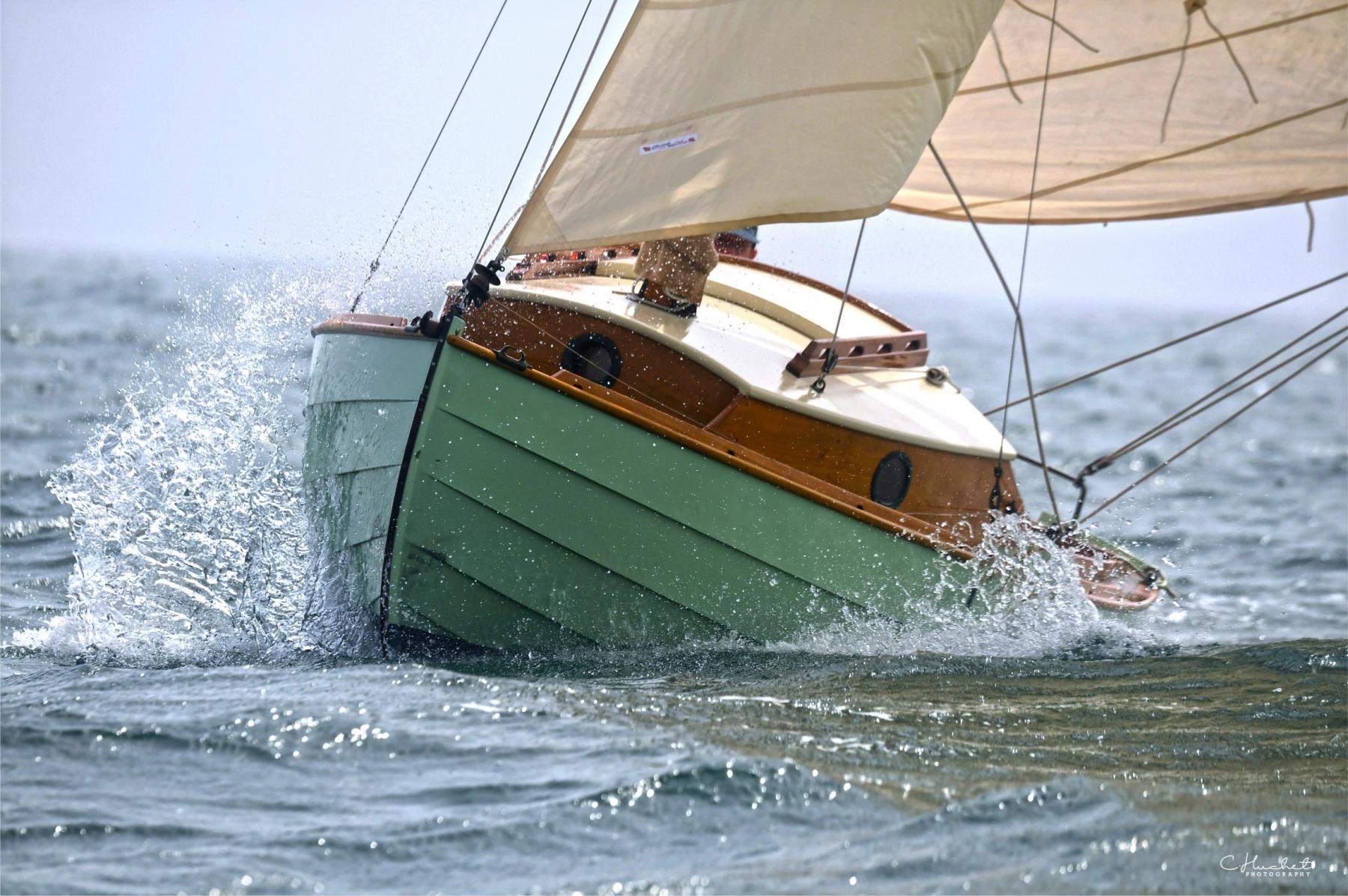 Vieux gréement en bois vert fendant l’écume, voiles claires gonflées par le vent, gerbe d’eau dynamique latérale.