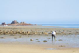 Pêcheur à pied en bottes sur l’estran sablonneux de Port Blanc à marée basse sous un ciel bleu limpide.