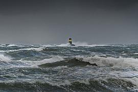 Vagues puissantes et écume blanche entourant la balise jaune et noire Nerput à Saint-Lunaire sous un ciel de tempête sombre.