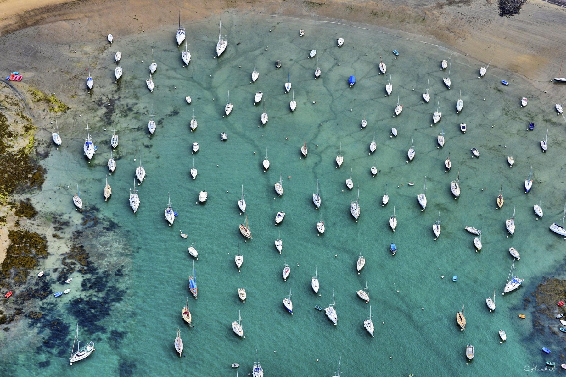 Vue aérienne plongeante de dizaines de bateaux blancs ancrés dans les eaux claires de la plage du Béchet à Saint-Briac.