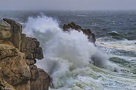 Vague massive d’écume blanche explosant sur les rochers du Croisic sous un ciel de tempête grisâtre et agité.