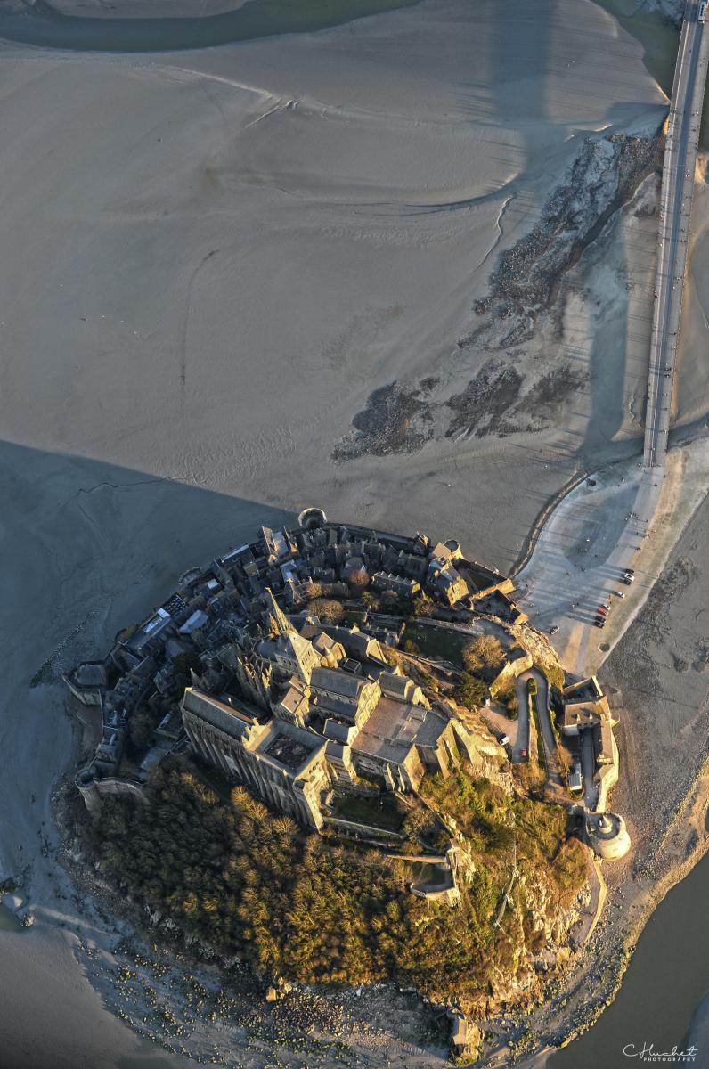 Vue verticale en plongée du Mont Saint-Michel, abbaye et remparts sur fond de sable strié par la marée basse.