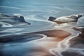 Méandres d’eau sur le sable en Baie du Mont Saint-Michel, reflets bleus et dorés, vue aérienne graphique.