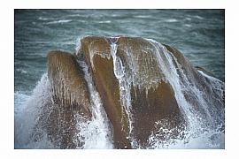 Rocher anthropomorphe frappé par l’écume en mer d’Iroise. Eau ruisselante sur le granit sous une lumière naturelle diffuse.