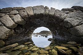 Arche en pierres de granit à Saint-Briac-sur-Mer encadrant une vue sur l’estran rocheux et l’eau à marée basse.