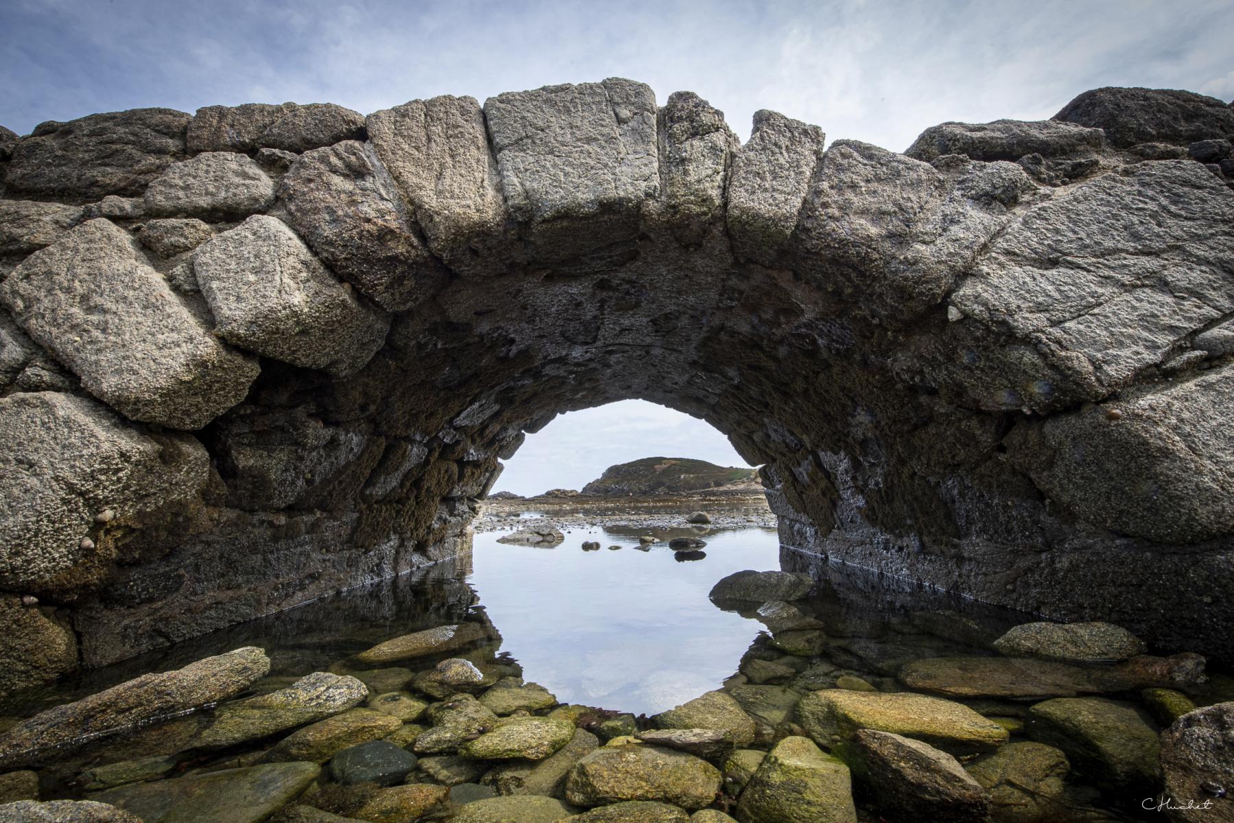Arche en pierres de granit à Saint-Briac-sur-Mer encadrant une vue sur l’estran rocheux et l’eau à marée basse.