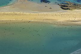 Vue aérienne d’un banc de sable clair entouré d’eau turquoise et de rochers sombres aux îles Ebihens.
