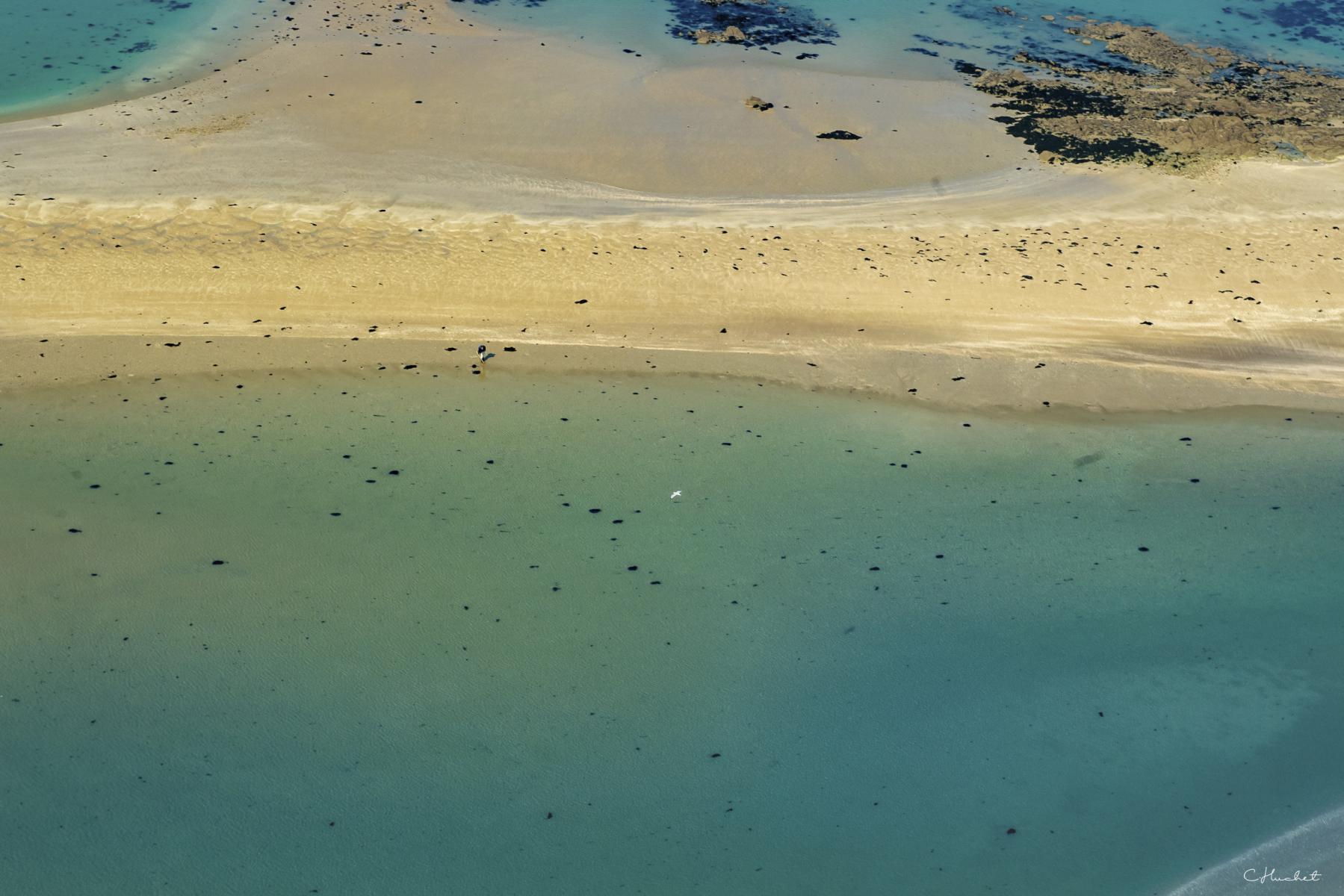 Vue aérienne d’un banc de sable clair entouré d’eau turquoise et de rochers sombres aux îles Ebihens.