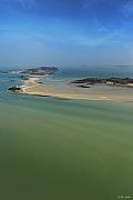 Vue aérienne de mer émeraude translucide, bancs de sable blanc et îlots rocheux bretons sous un ciel bleu dégagé.