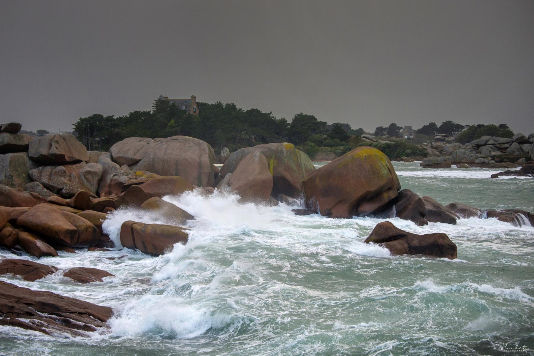 Vagues écumantes sur les rochers de granit rose à Ploumanac’h sous un ciel d’orage gris en Bretagne.