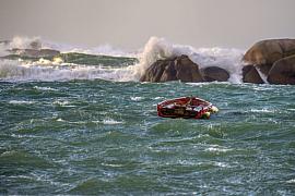 Barque rouge sur mer agitée avec vagues sur rochers de granit rose à Trégastel par temps couvert.