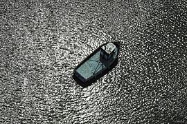 Vue plongeante d’un chalutier sur une eau aux reflets argentés scintillants. Coque détaillée et contrastée à Saint-Armel.