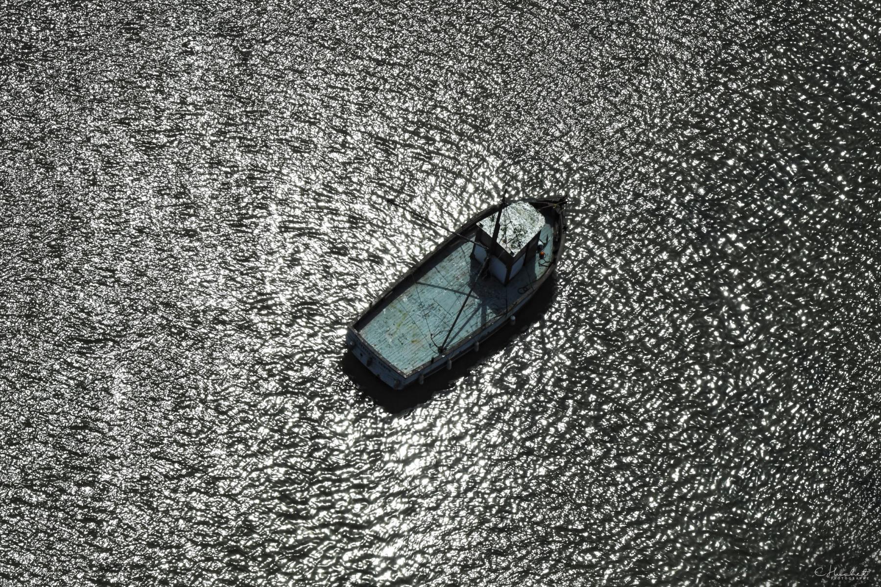 Vue plongeante d’un chalutier sur une eau aux reflets argentés scintillants. Coque détaillée et contrastée à Saint-Armel.