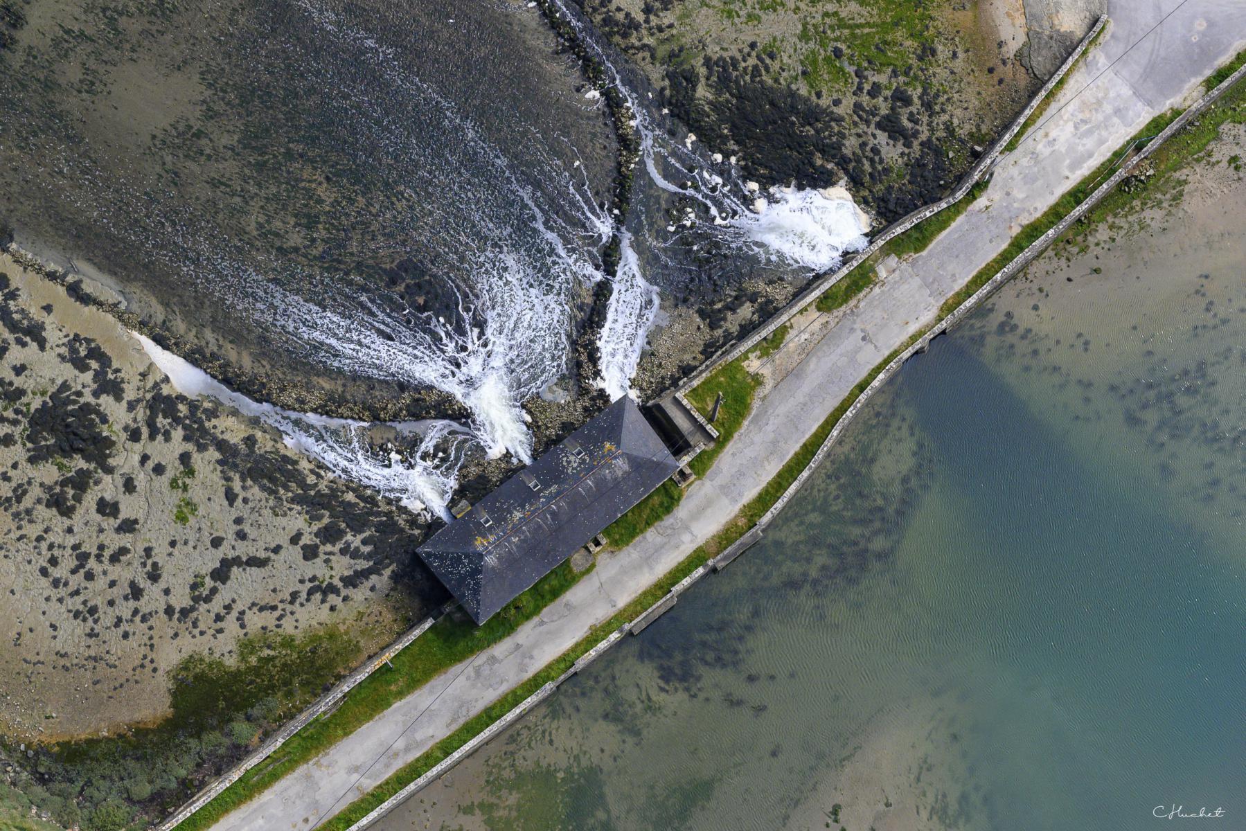 Vue zénithale d’un moulin à marée en pierre avec l’eau s’écoulant par les vannes d’une digue dans le Morbihan en Bretagne.