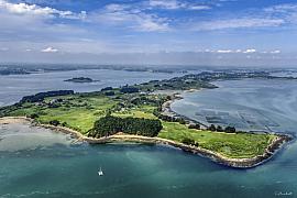 Vue aérienne de l’Ile aux Moines montrant les côtes, la végétation et les eaux du Golfe du Morbihan sous un ciel bleu.