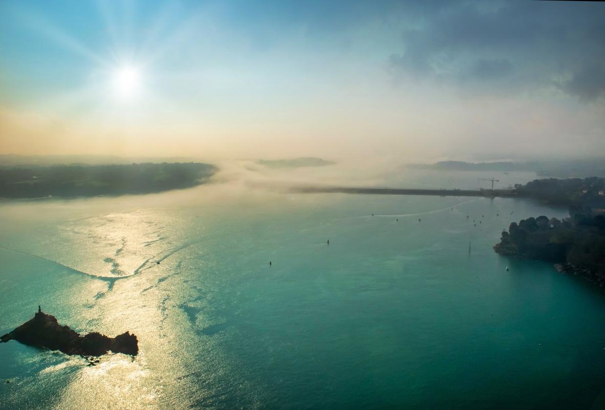 Vue aérienne du barrage de la Rance sous la brume avec reflets solaires sur mer turquoise à Dinard.