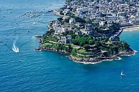 Vue aérienne de la Pointe du Moulinet à Dinard, villas côtières et bateaux naviguant sur une mer émeraude.