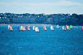 Voiliers aux spinnakers colorés naviguant devant le front de mer et la plage de l’Écluse à Dinard.