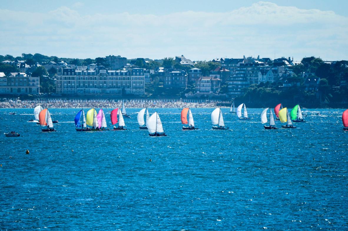Voiliers aux spinnakers colorés naviguant devant le front de mer et la plage de l’Écluse à Dinard.