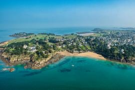 Vue aérienne de la plage de la Petite Salinette à Saint-Briac, eaux turquoises et côtes rocheuses sous un ciel dégagé.
